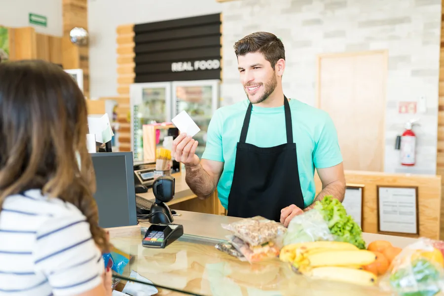 Shop assistant at a till handing a plastic loyalty card to a customer